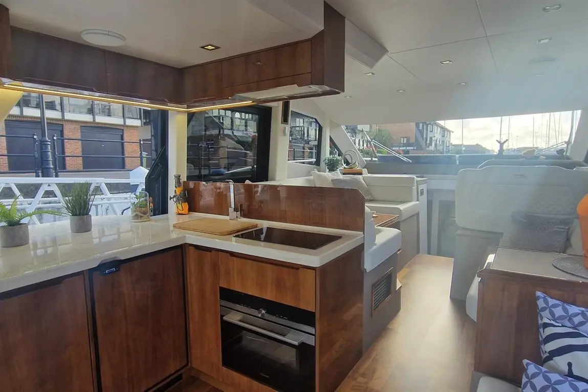 Modern yacht interior featuring a kitchen with wooden cabinets, marble countertops, and a view of the marina outside.